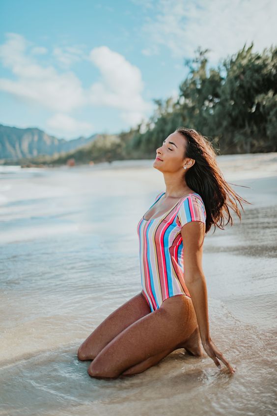 Woman kneeling on the beech in a striped bathing suit