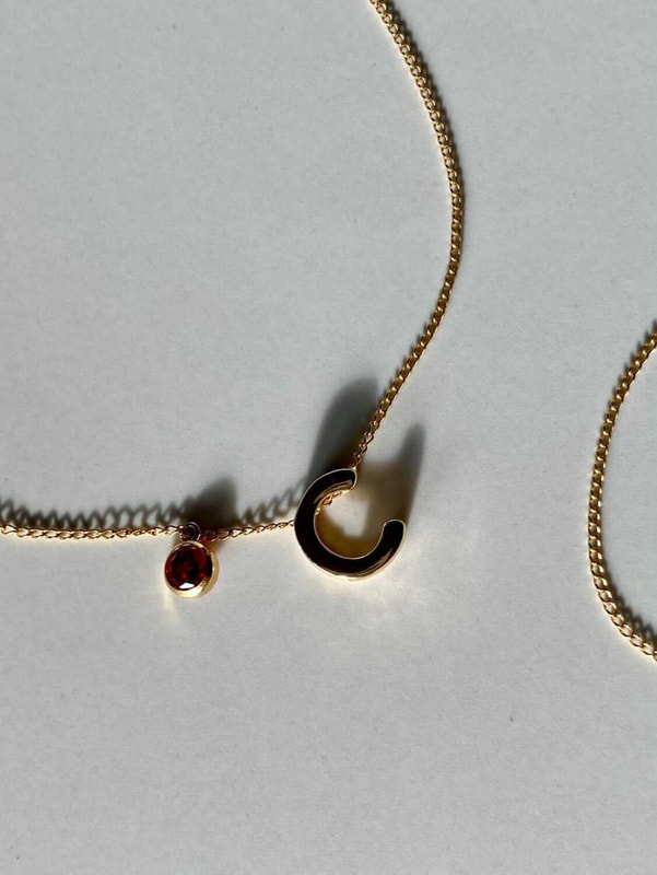 Gold necklace with the initial letter C and a ruby birthstone for July.