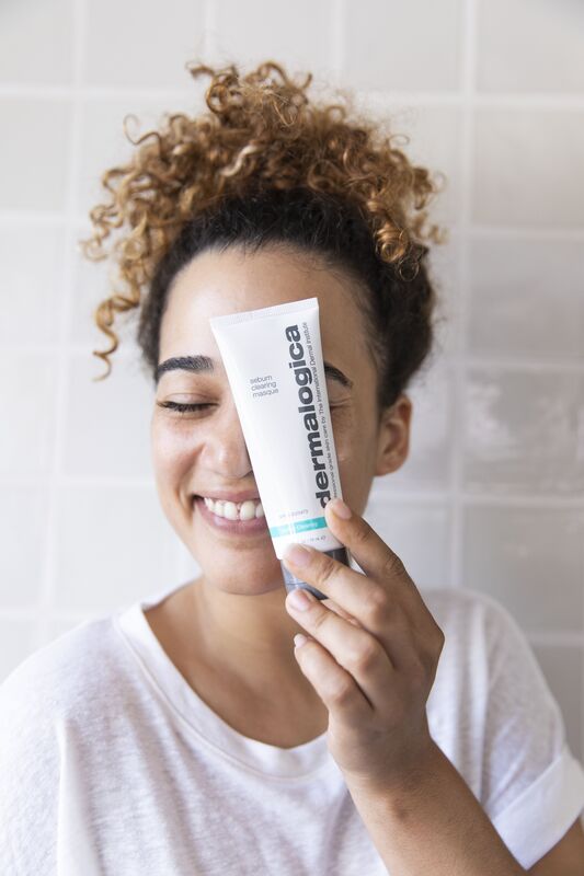 Girl holding dermalogica skincare product in front of her face and smiling